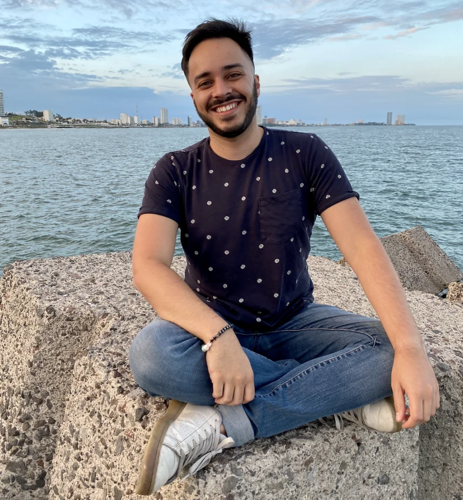 Teacher Zachary smiling while sitting on rocks by the sea