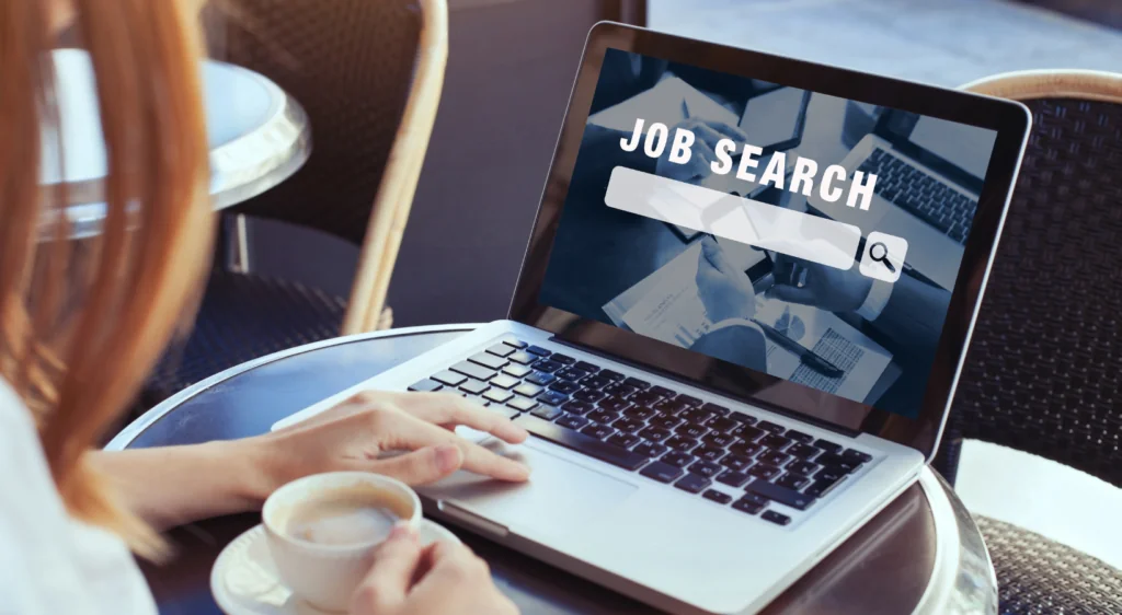Laptop mostrando una búsqueda de empleo mientras una persona toma un café