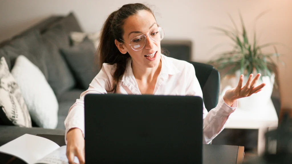 Teacher with glasses talking and gesturing in front of her laptop