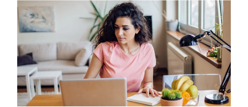 Mujer sentada en un escritorio mirando la pantalla de su laptop en una sala luminosa