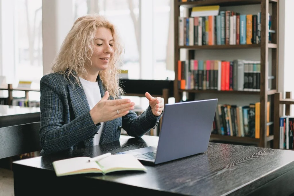 Blonde woman gesturing in front of her laptop on a video call